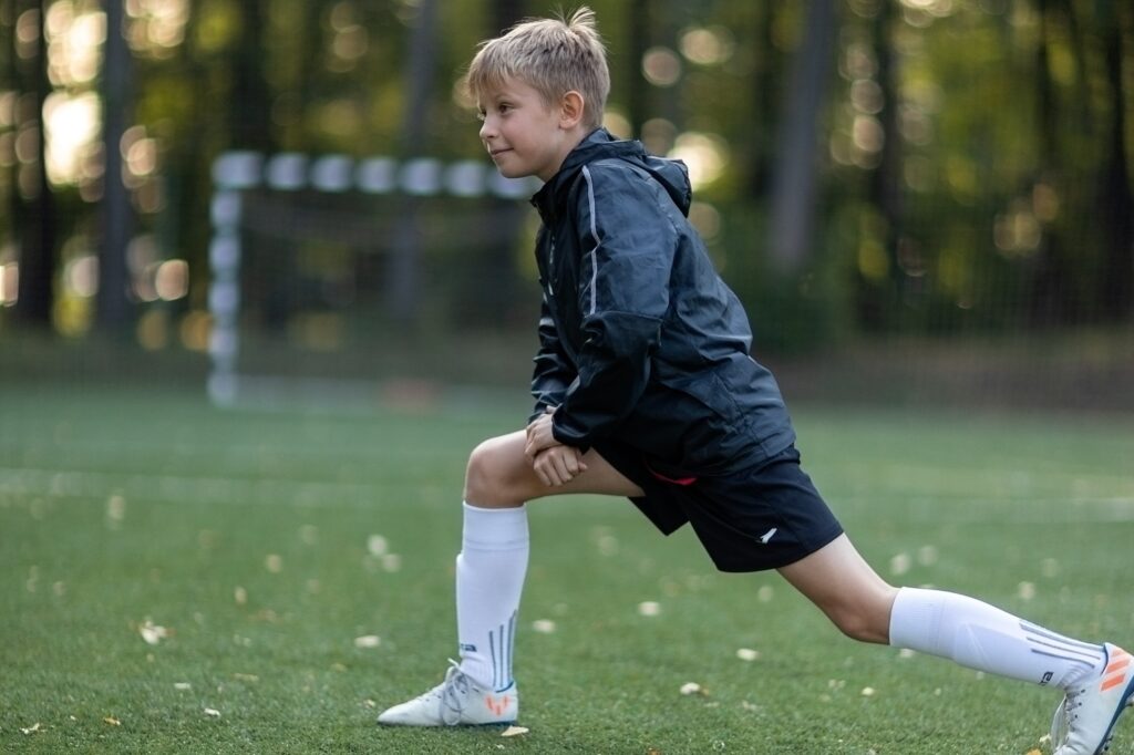 A kid doing his stretches on a football pitch